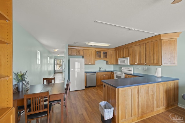 kitchen with white appliances, kitchen peninsula, hardwood / wood-style floors, and sink