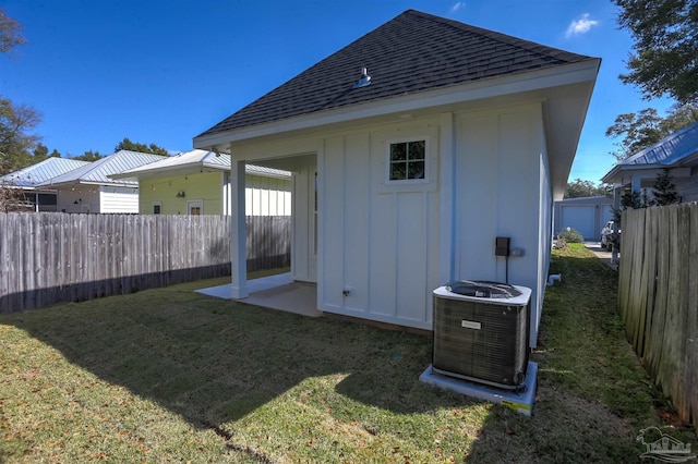 back of property with central AC unit, roof with shingles, a yard, an outdoor structure, and board and batten siding