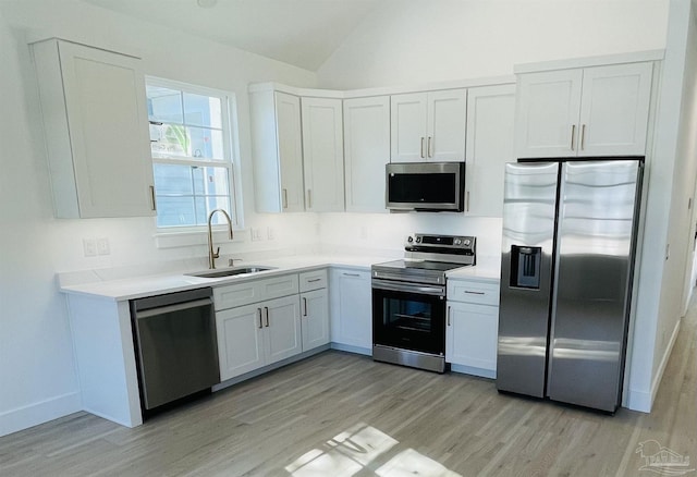 kitchen with white cabinets, lofted ceiling, appliances with stainless steel finishes, light countertops, and a sink