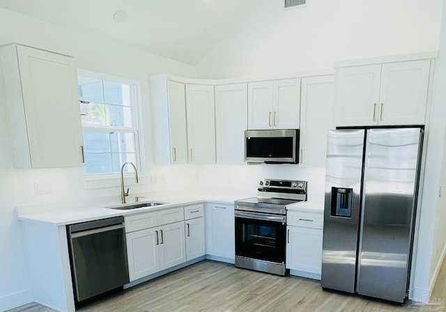 kitchen with vaulted ceiling, light hardwood / wood-style floors, white cabinetry, appliances with stainless steel finishes, and sink