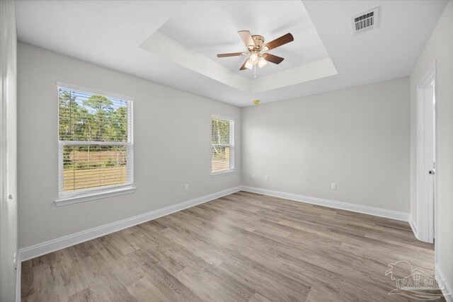 unfurnished room with light hardwood / wood-style floors, a healthy amount of sunlight, a raised ceiling, and ceiling fan