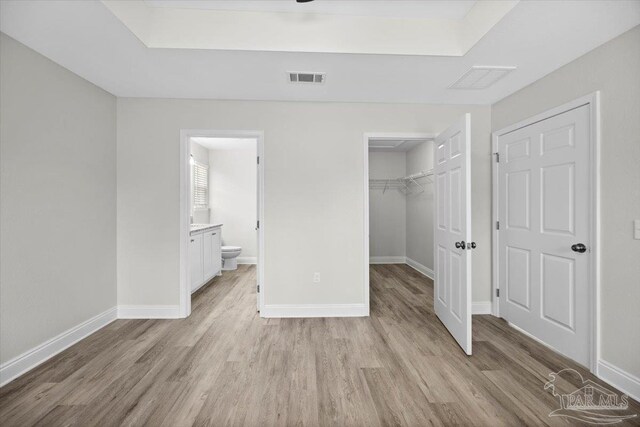 unfurnished bedroom with light hardwood / wood-style floors, a walk in closet, ensuite bath, and a closet