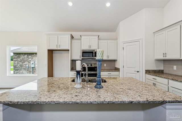 kitchen featuring a sink, light stone counters, stainless steel microwave, and a center island with sink