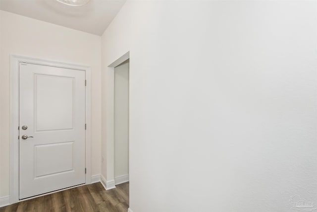 corridor featuring baseboards and dark wood-type flooring