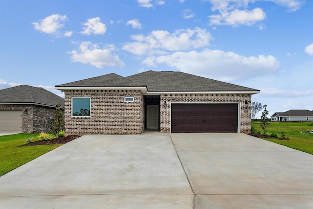 prairie-style home featuring a shingled roof, an attached garage, a front lawn, brick siding, and driveway