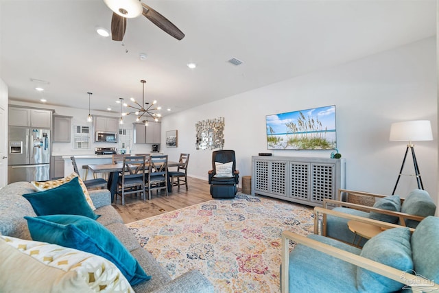 living room featuring light wood finished floors, recessed lighting, visible vents, baseboards, and ceiling fan with notable chandelier