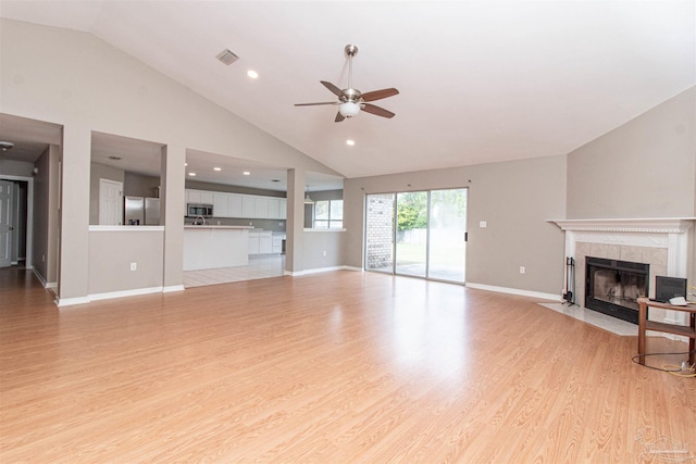 unfurnished living room with a fireplace, high vaulted ceiling, light wood-type flooring, and ceiling fan