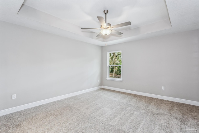 carpeted spare room featuring a raised ceiling and ceiling fan