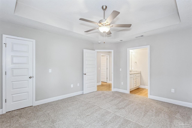 unfurnished bedroom featuring connected bathroom, light carpet, ceiling fan, and a tray ceiling