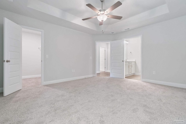 unfurnished bedroom featuring light carpet, a tray ceiling, and ceiling fan