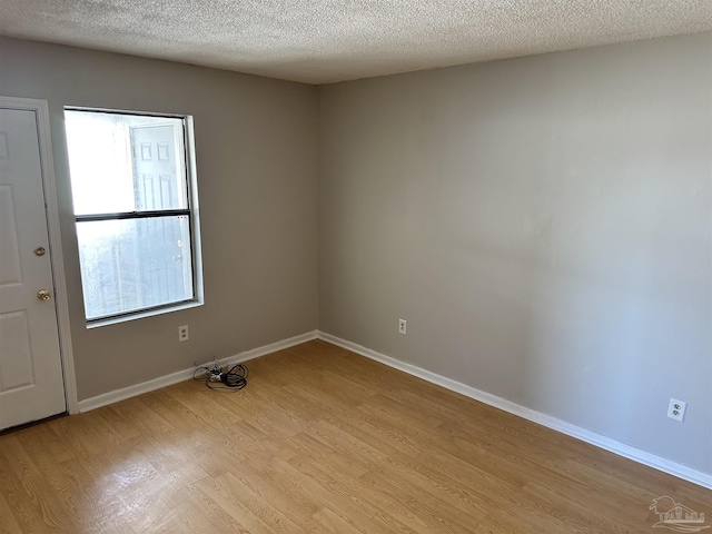 spare room with a textured ceiling, a wealth of natural light, and light hardwood / wood-style floors