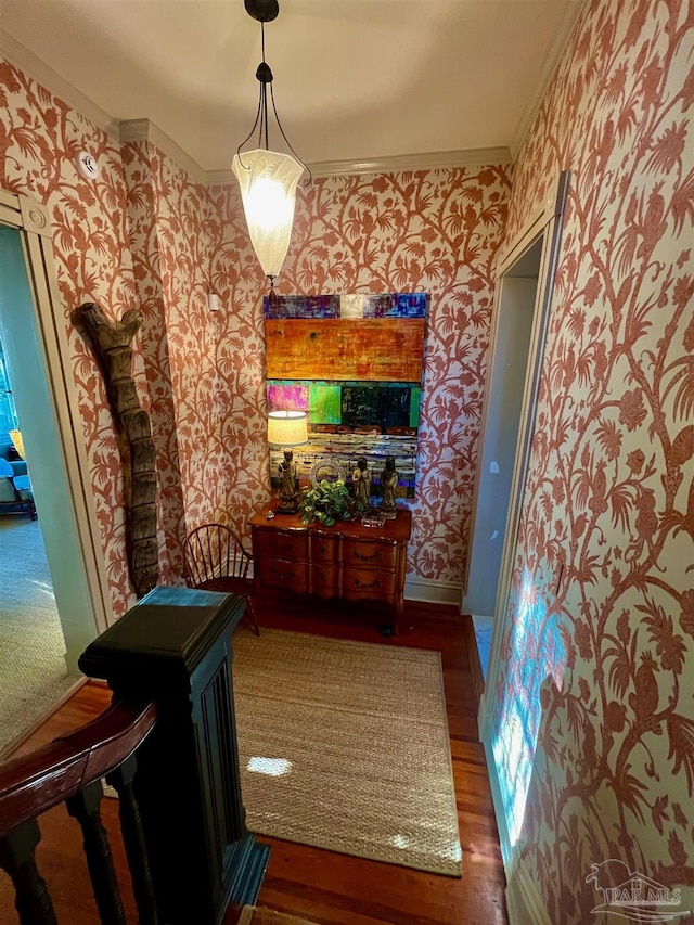 hall with dark wood-type flooring, ornamental molding, baseboards, and wallpapered walls