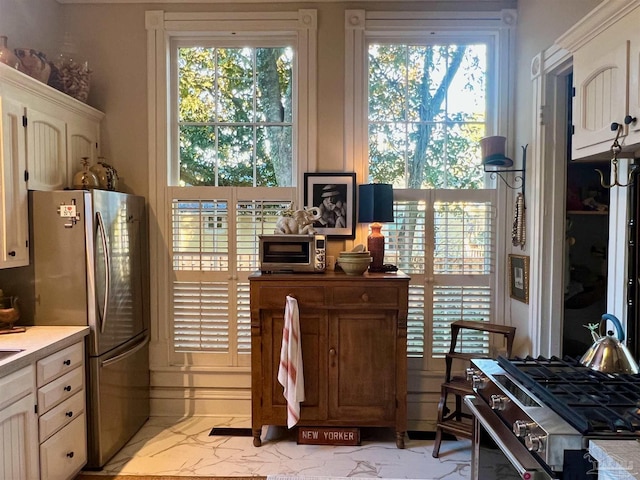 kitchen featuring appliances with stainless steel finishes, a wealth of natural light, marble finish floor, and light countertops