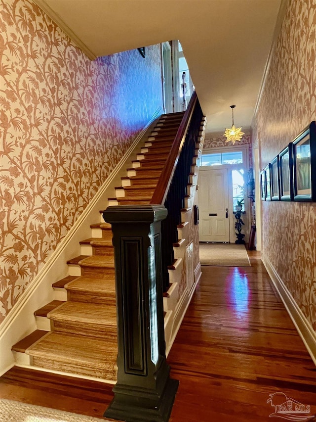 staircase with a chandelier, ornamental molding, wood finished floors, and wallpapered walls