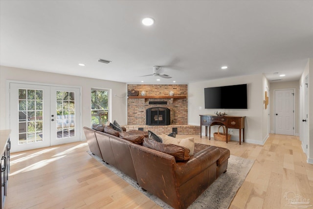 living room featuring a fireplace, ceiling fan, french doors, and light wood-type flooring