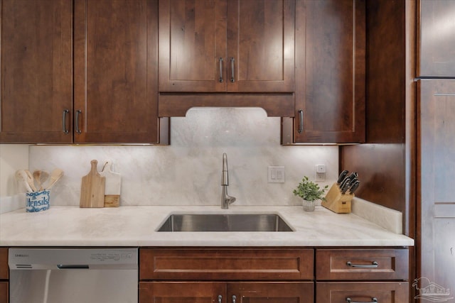 kitchen featuring stainless steel dishwasher, backsplash, light stone counters, and sink