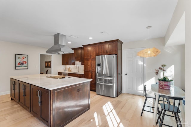 kitchen featuring stainless steel refrigerator with ice dispenser, a kitchen island, light wood-type flooring, decorative light fixtures, and island range hood