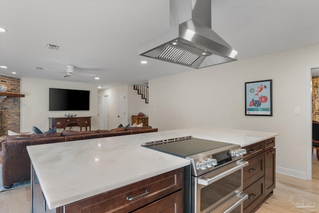 kitchen featuring ceiling fan, exhaust hood, a fireplace, stainless steel stove, and a kitchen island