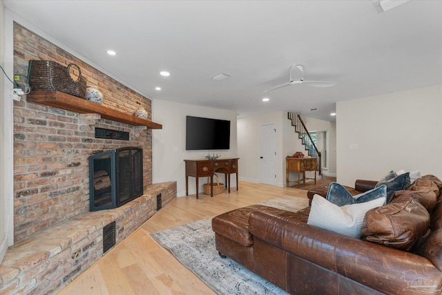 living room featuring ceiling fan, light hardwood / wood-style flooring, and a brick fireplace