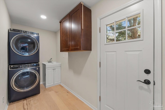 laundry room featuring cabinets, stacked washing maching and dryer, light hardwood / wood-style flooring, and sink