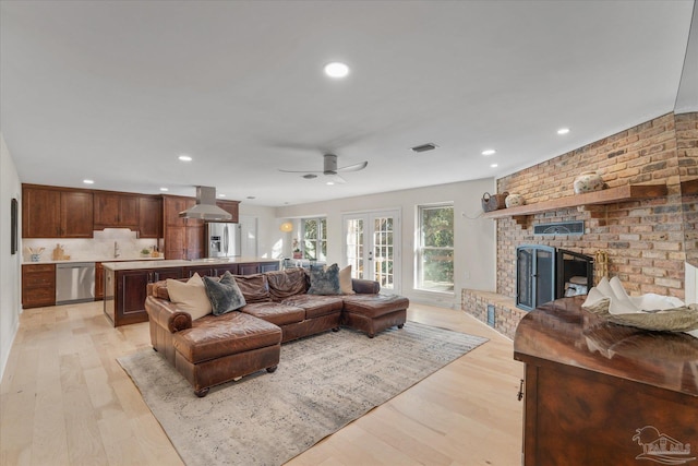 living room featuring ceiling fan, light hardwood / wood-style floors, a fireplace, and french doors