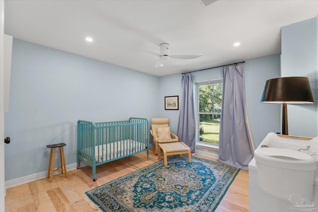 bedroom featuring ceiling fan, wood-type flooring, and a crib