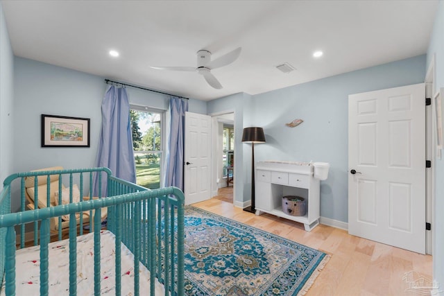 bedroom with ceiling fan, light wood-type flooring, and a nursery area