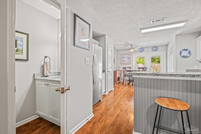 kitchen with a breakfast bar area, stainless steel fridge, light wood-type flooring, white cabinetry, and ceiling fan