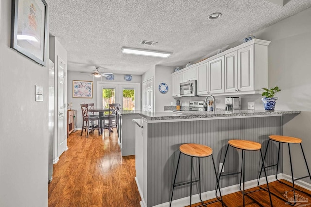 kitchen with light hardwood / wood-style floors, kitchen peninsula, white cabinetry, and a breakfast bar area