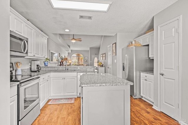 kitchen featuring appliances with stainless steel finishes, light hardwood / wood-style flooring, and white cabinetry