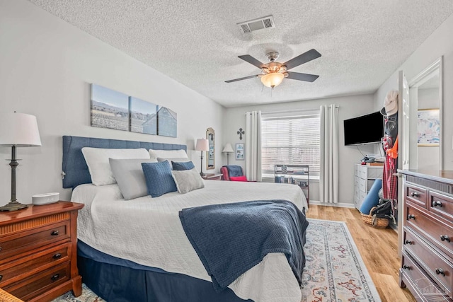 bedroom with light hardwood / wood-style flooring, a textured ceiling, and ceiling fan