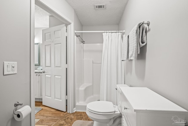 bathroom featuring hardwood / wood-style floors, a textured ceiling, walk in shower, toilet, and vanity