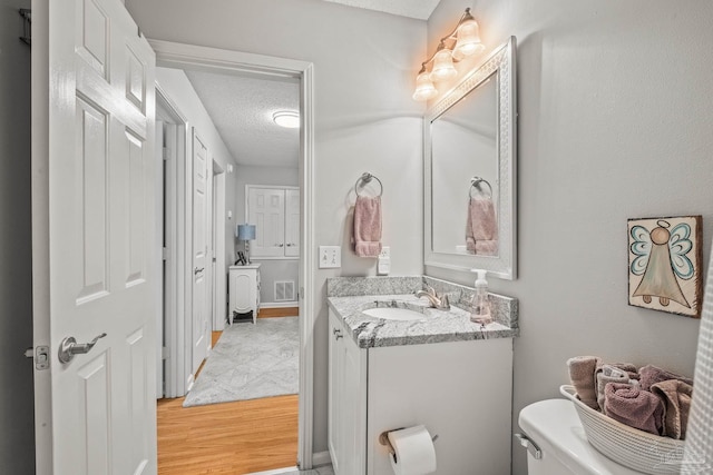 bathroom featuring vanity, a textured ceiling, wood-type flooring, and toilet