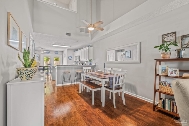 dining space featuring hardwood / wood-style floors, ceiling fan, a textured ceiling, a towering ceiling, and french doors