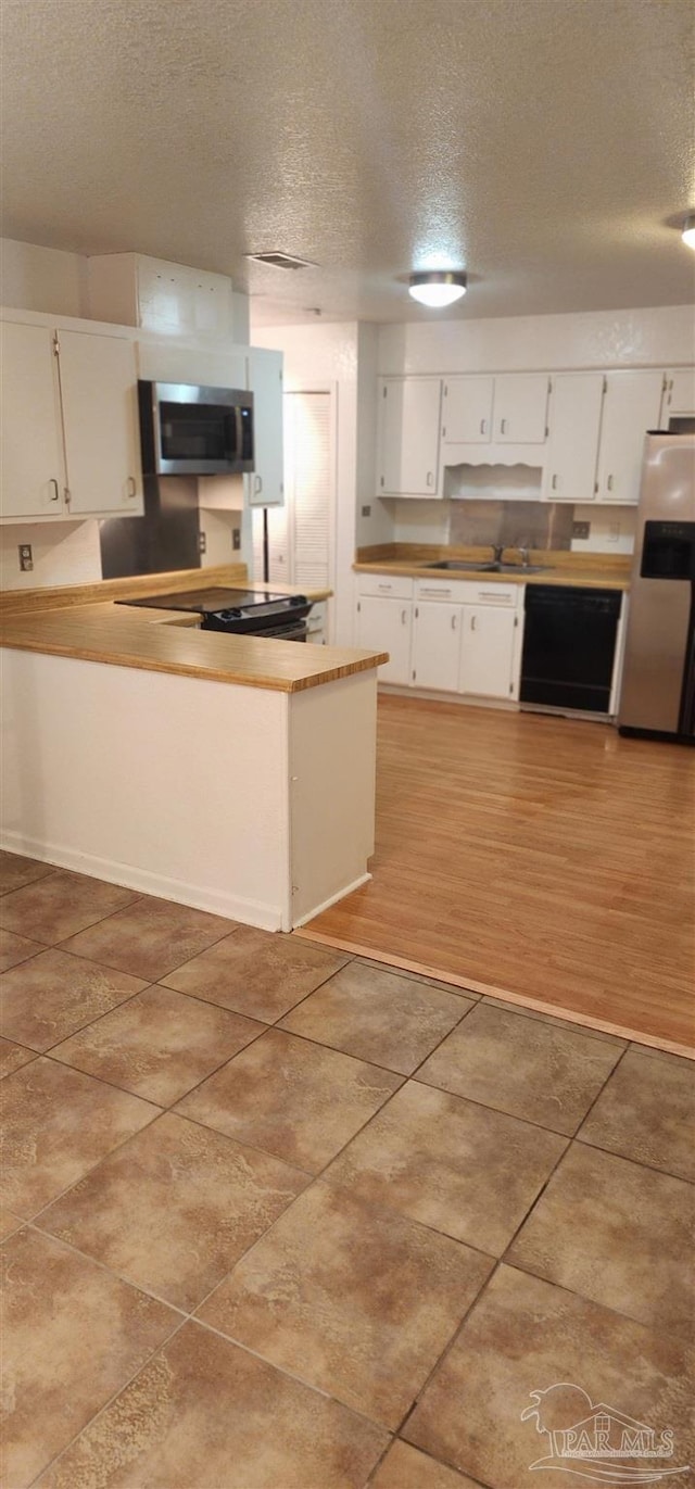 kitchen with white cabinetry, appliances with stainless steel finishes, light tile patterned floors, and a textured ceiling