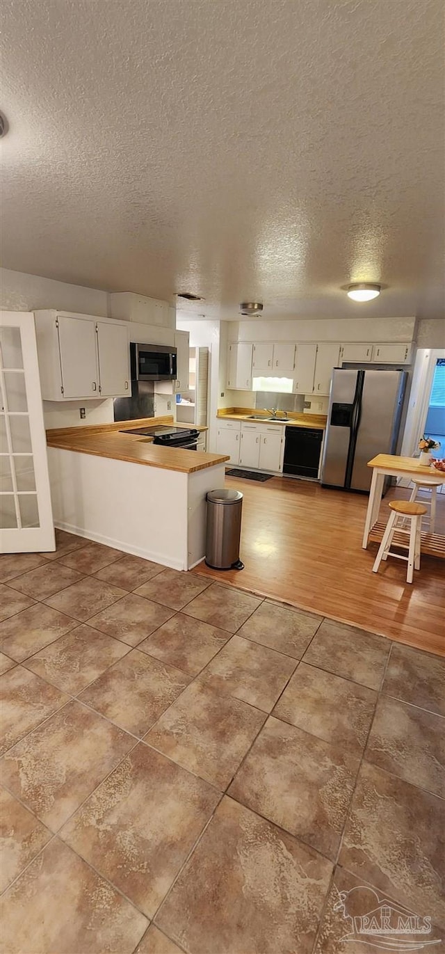 kitchen with appliances with stainless steel finishes, kitchen peninsula, a textured ceiling, and white cabinets