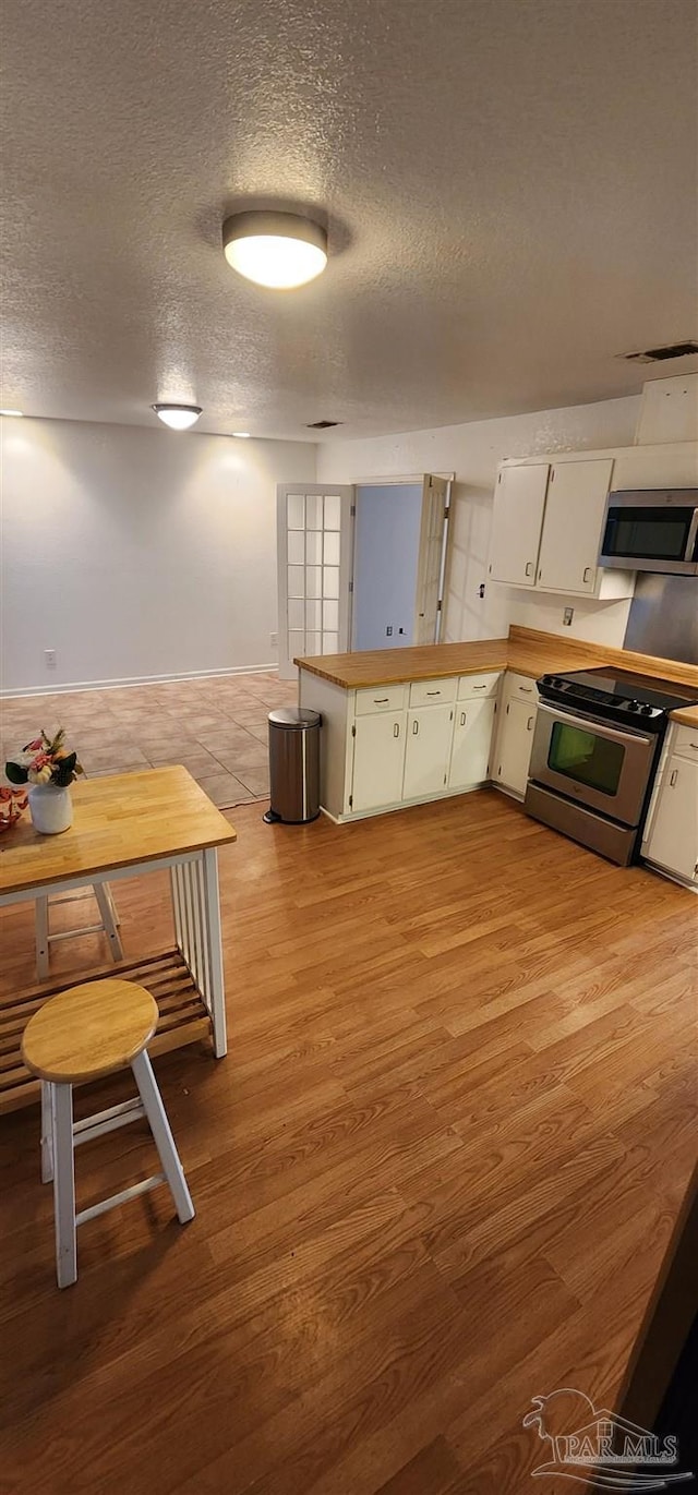 kitchen featuring light hardwood / wood-style flooring, appliances with stainless steel finishes, a textured ceiling, white cabinets, and kitchen peninsula