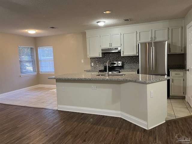 kitchen with decorative backsplash, a kitchen island with sink, sink, white cabinets, and tile patterned flooring