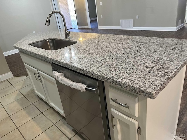 kitchen with a kitchen island with sink, sink, stainless steel dishwasher, light stone countertops, and light tile patterned floors