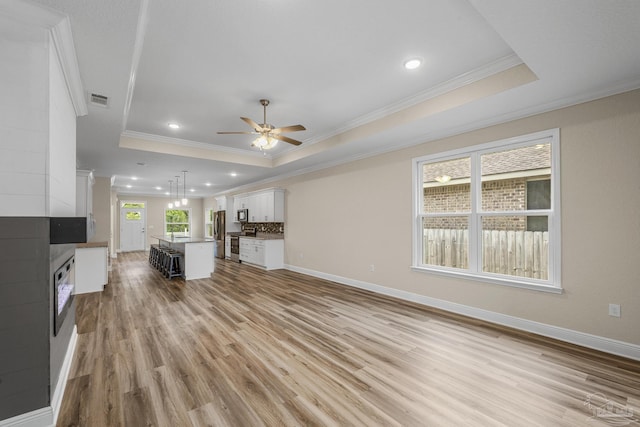 unfurnished living room featuring a tile fireplace, a ceiling fan, a tray ceiling, and light wood-type flooring