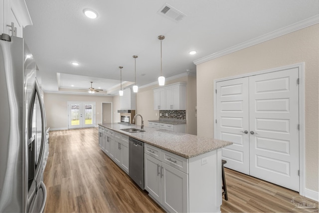 kitchen with a kitchen island with sink, appliances with stainless steel finishes, light wood-style flooring, ornamental molding, and visible vents