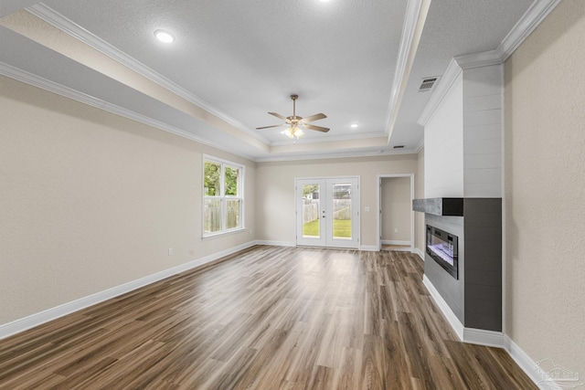 unfurnished living room featuring dark wood-style floors, a tray ceiling, visible vents, a ceiling fan, and crown molding