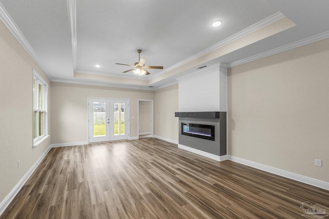 unfurnished living room with a ceiling fan, wood finished floors, a large fireplace, a tray ceiling, and visible vents