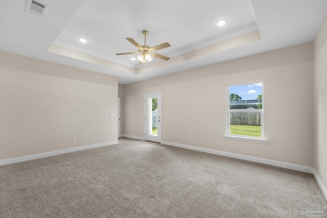 carpeted empty room with a tray ceiling, visible vents, crown molding, baseboards, and ceiling fan
