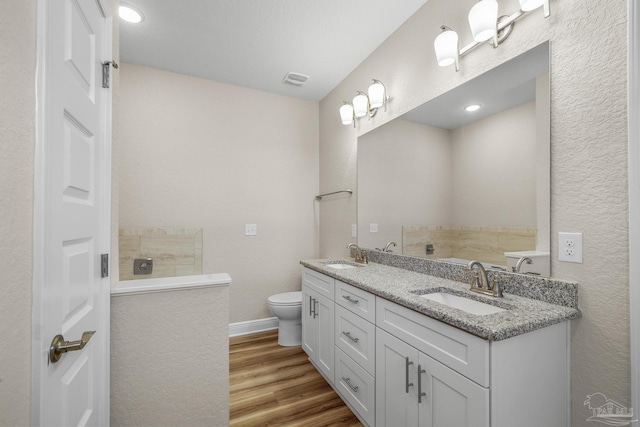 full bath featuring double vanity, wood finished floors, toilet, and a sink