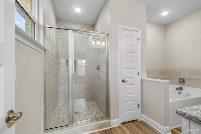 bathroom with a garden tub, wood finished floors, a stall shower, vanity, and baseboards