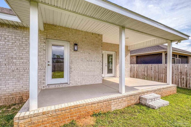 doorway to property featuring brick siding, fence, and a patio area