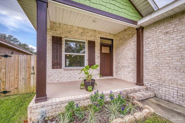 entrance to property with brick siding, a porch, and fence