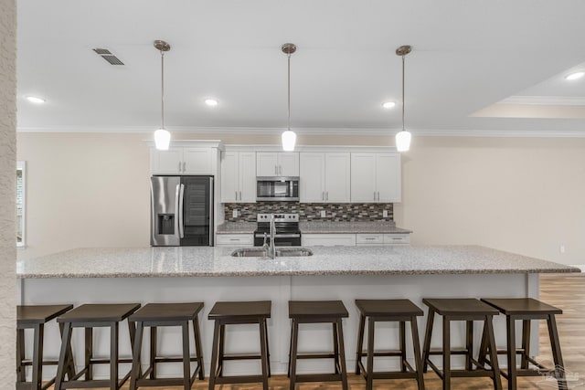 kitchen with stainless steel appliances, a kitchen breakfast bar, a sink, tasteful backsplash, and white cabinetry
