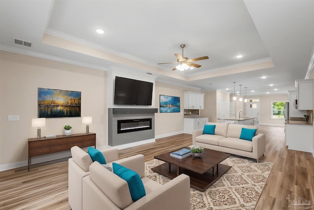 living area featuring ceiling fan, light wood finished floors, visible vents, and a raised ceiling